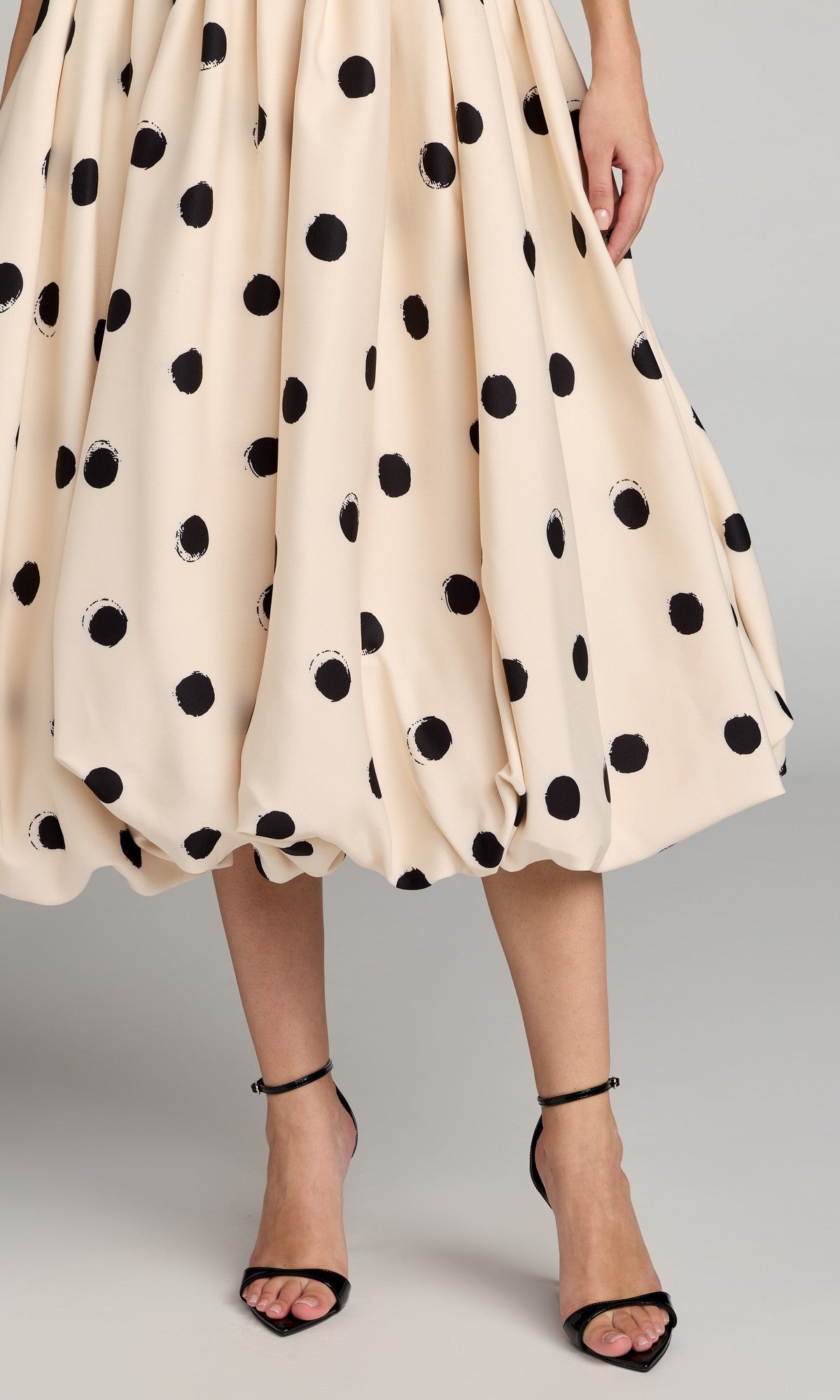 A person wearing the Mac Duggal 21234 Semi-Formal Polka Dot Midi Dress with a cream fit-and-flare silhouette and A-line skirt, paired with black high-heeled sandals, stands against a plain background.